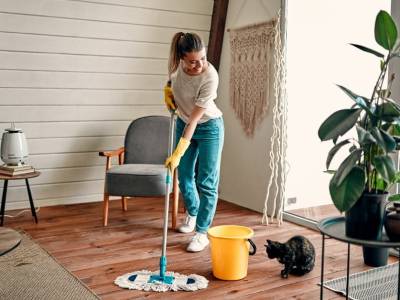 Woman smiling at a black cat sitting on the floor while cleaning the house with a mop.