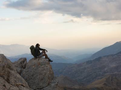 Male backpacker sitting on rock in mountains.