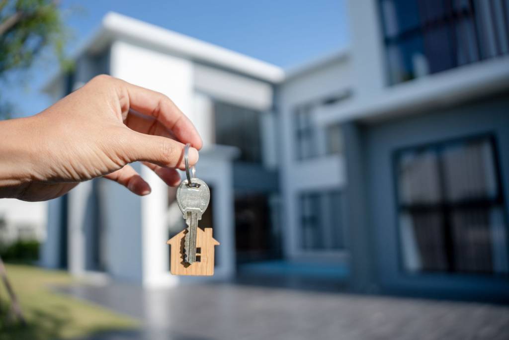 Person holding up a door key in front of their new home.