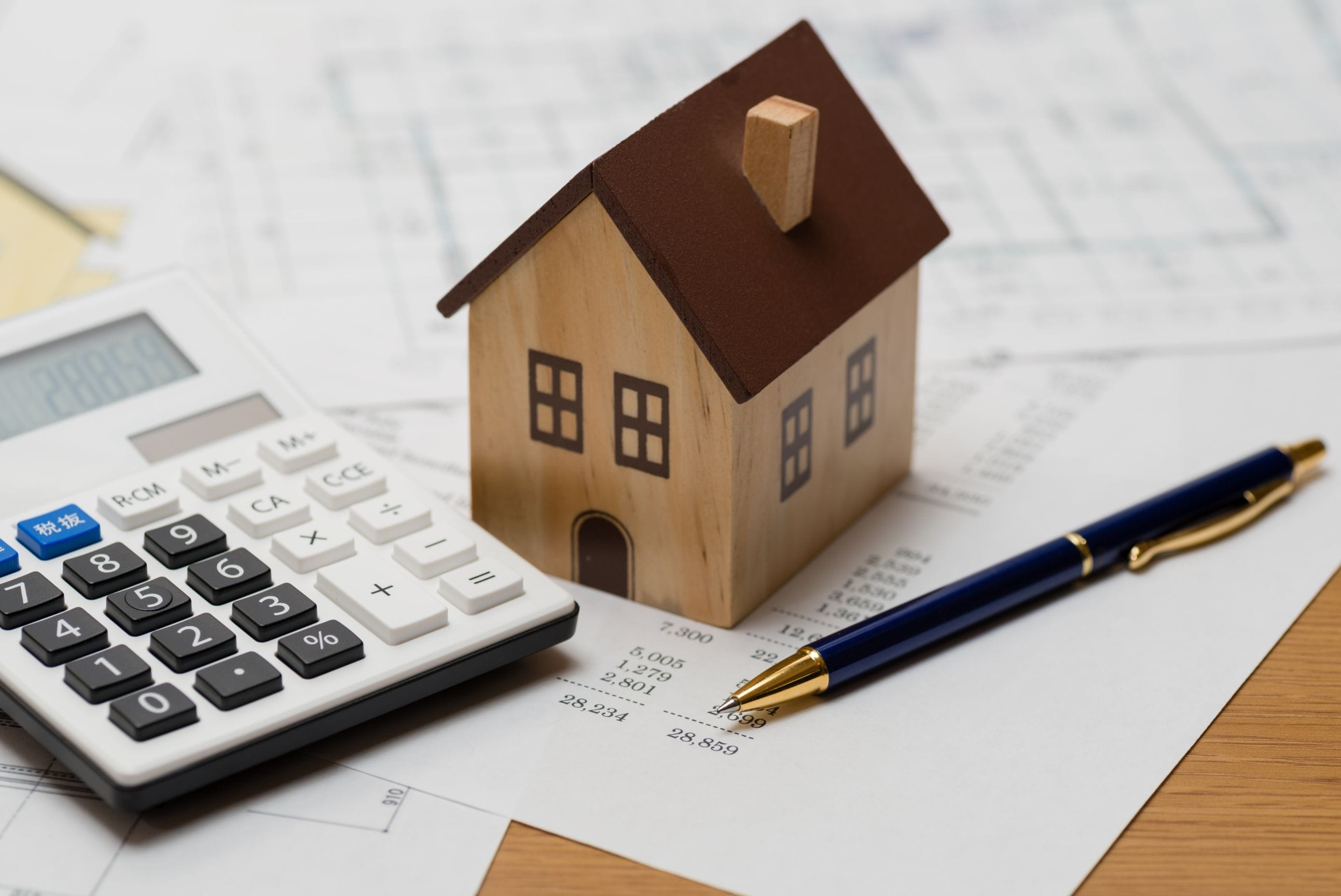 A calculator, pen and model house on a sheet detailing living costs.