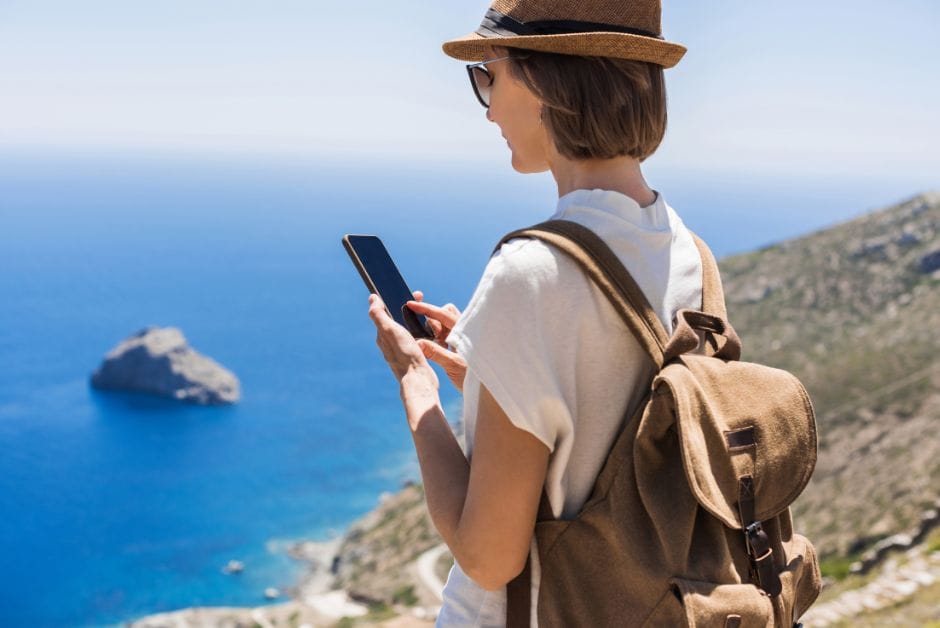 Female tourist using smart-tourism mobile app on coastal cliff.