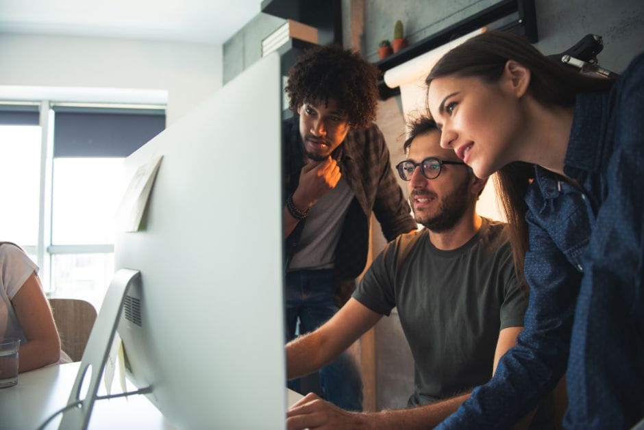 Tech startup team gathered around computer screen.