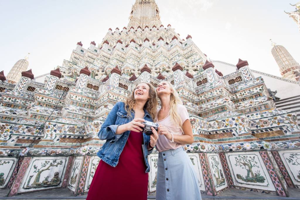 Two female tourists standing with a camera in front of a temple in Thailand.