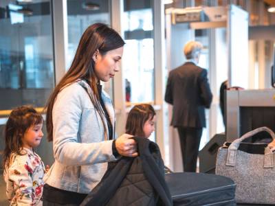 Female passenger loading baggage onto conveyor belt at airport X-ray machine.