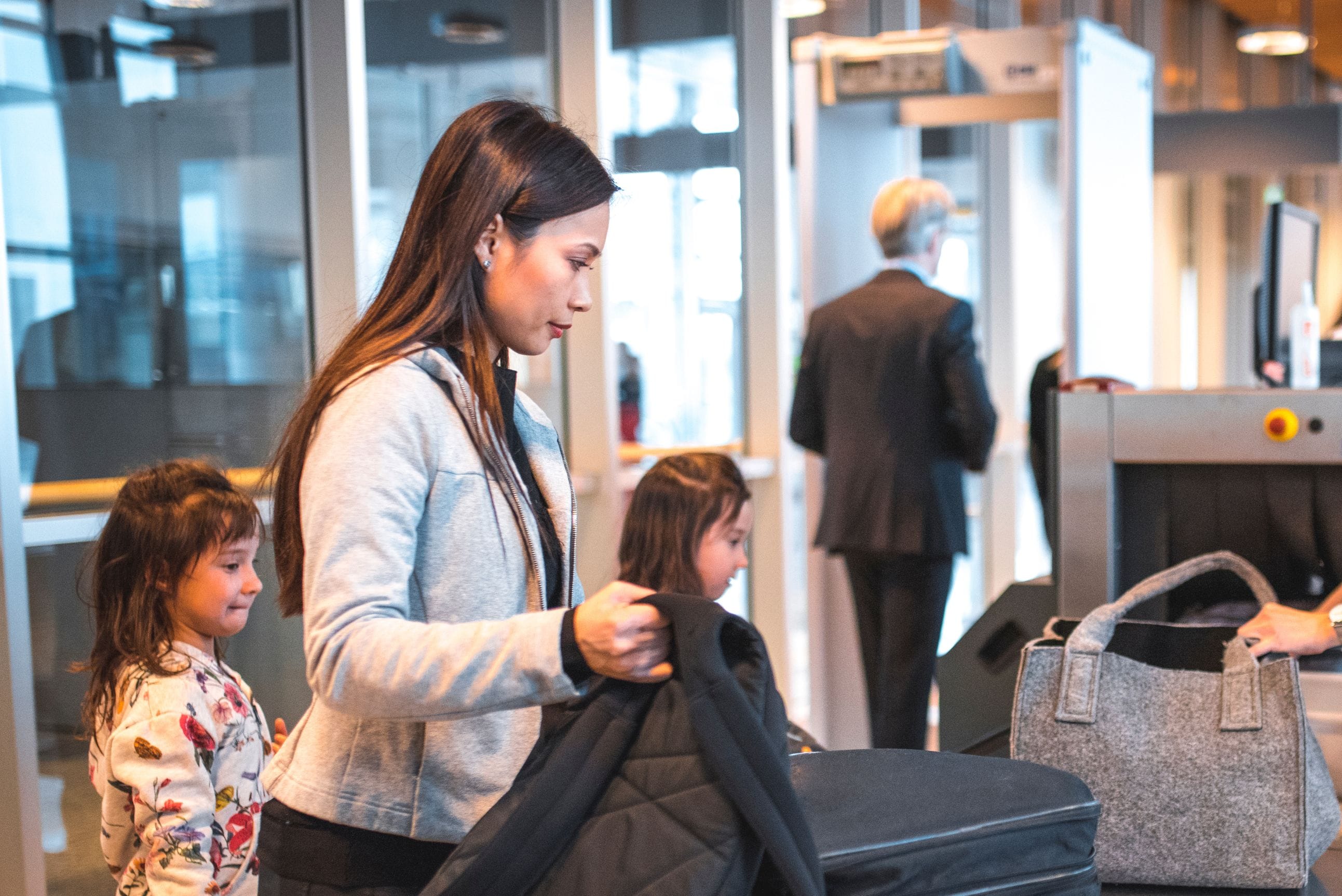 Female passenger loading baggage onto conveyor belt at airport X-ray machine.