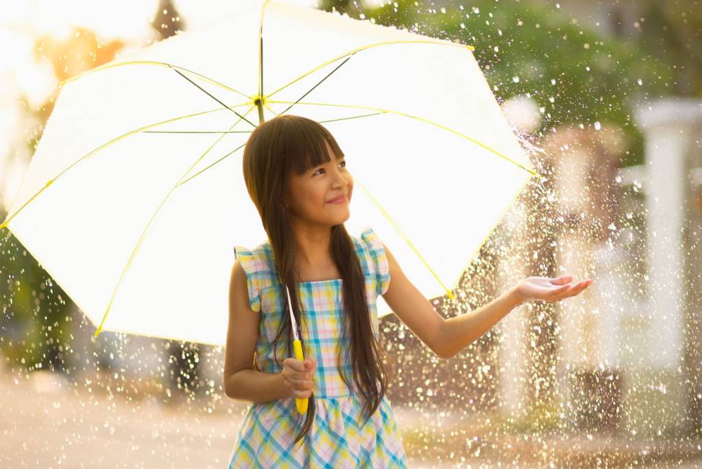 A smiling Asian girl holding an umbrella over herself in the rain.