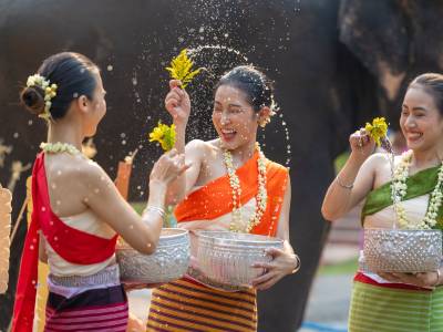 Women in traditional dress splashing each other with water during Songkran in Thailand.