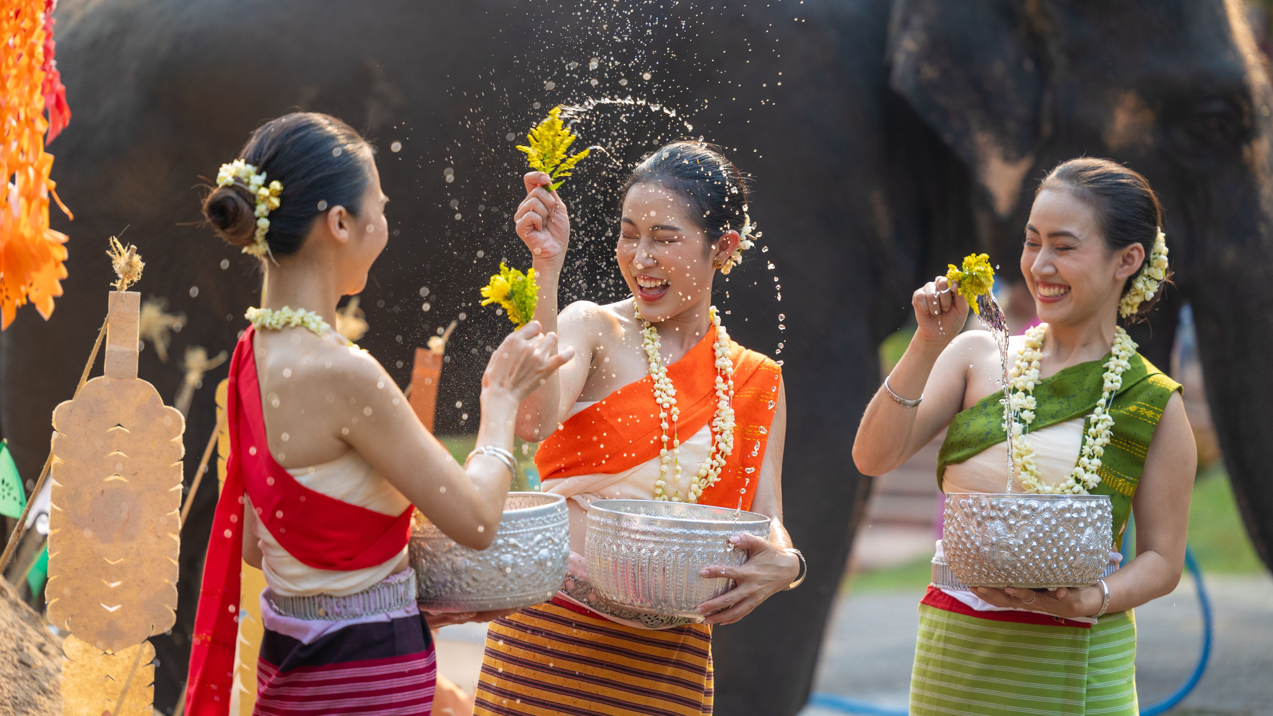 Women in traditional dress splashing each other with water during Songkran in Thailand.