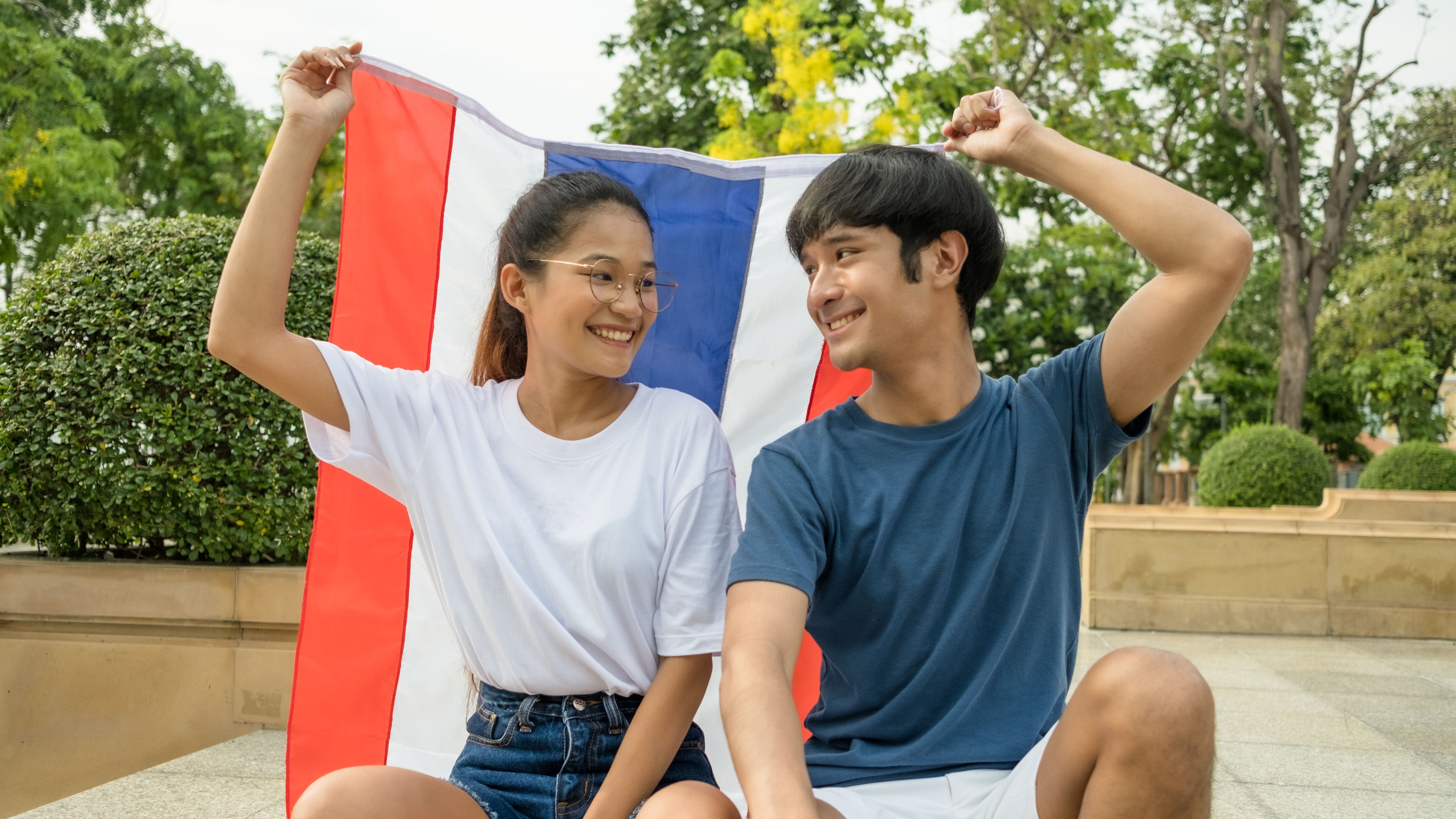 Two Thai teenagers holding up Thai flag together.