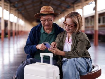 Two travelers sitting on train-station seat using their smartphone.