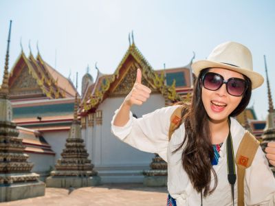 Female Asian tourist giving the thumbs-up in front of a temple.