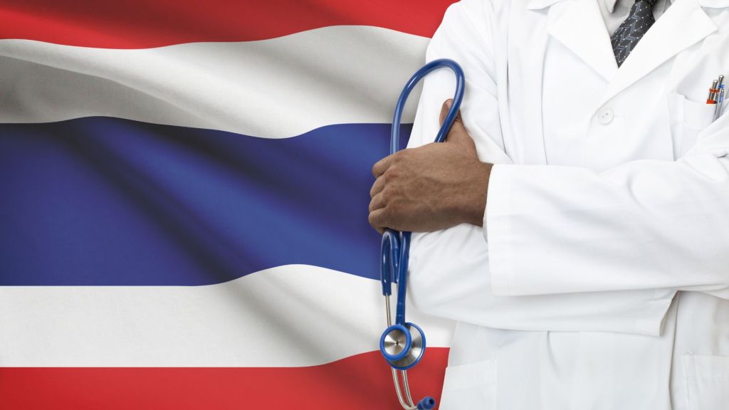Doctor holding stethoscope standing by flag of Thailand.