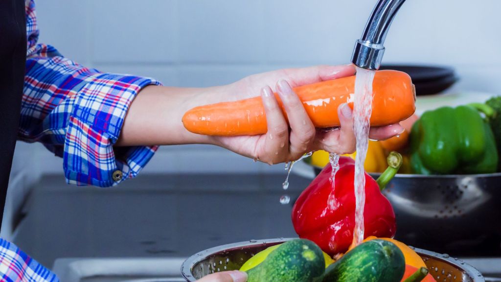 Close-up of a woman washing vegetables under a kitchen tap.