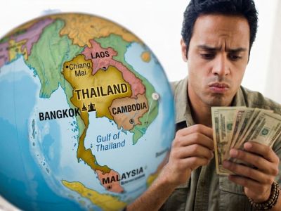 A man counts dollar bills next to a globe showing the country of Thailand.