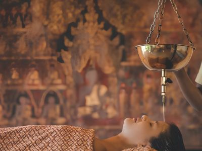 A woman is lying down receiving a shirodhara treatment at Kamalaya Wellness Sanctuary in Koh Samui.